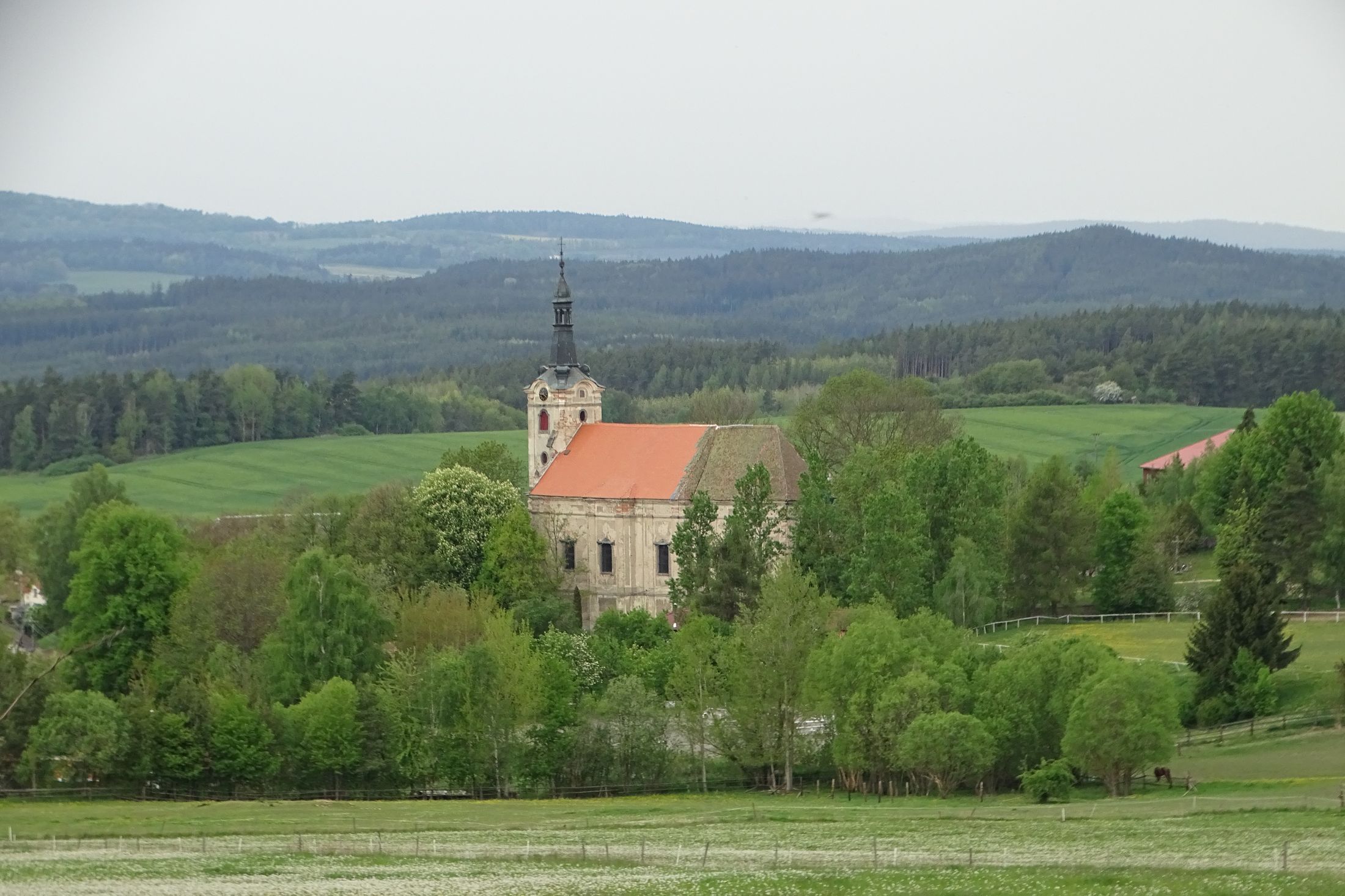Kostel zasazený do malebné krajiny, pohled z dálky.
